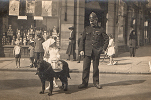 Charity collecting dog with a young girl crossing the street under the direction of a police officer