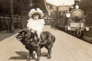 Charity collecting dog with a young girl at a train station in 1907